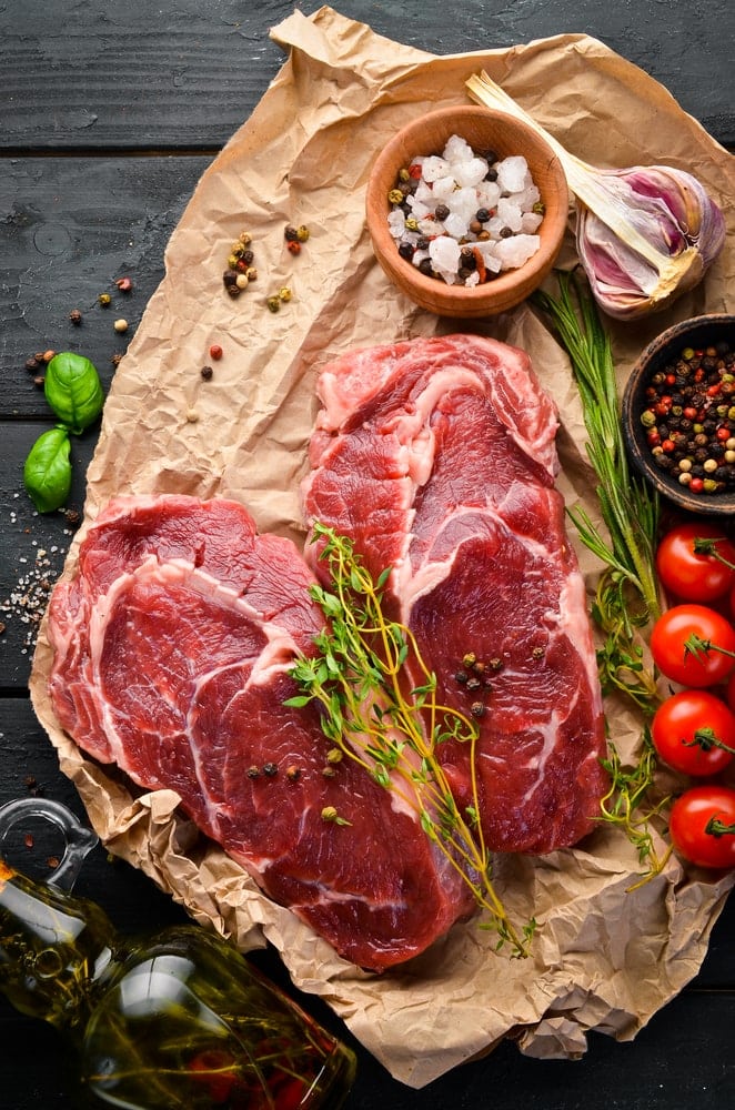 High quality steaks laid out with salt, tomatoes and garlic for cooking.